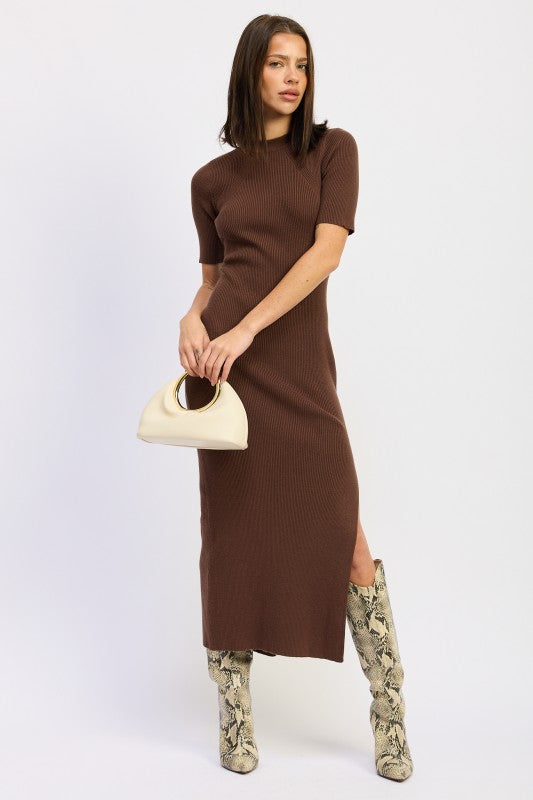 Woman wearing a ribbed knit sweater dress with side slit, styled with knee-high boots and minimalist accessories.