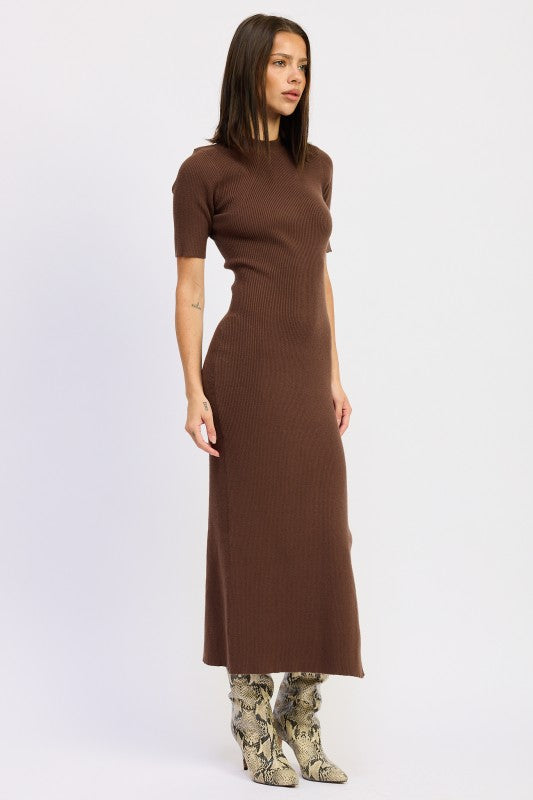 Woman wearing a ribbed knit sweater dress with side slit, styled with knee-high boots and minimalist accessories.