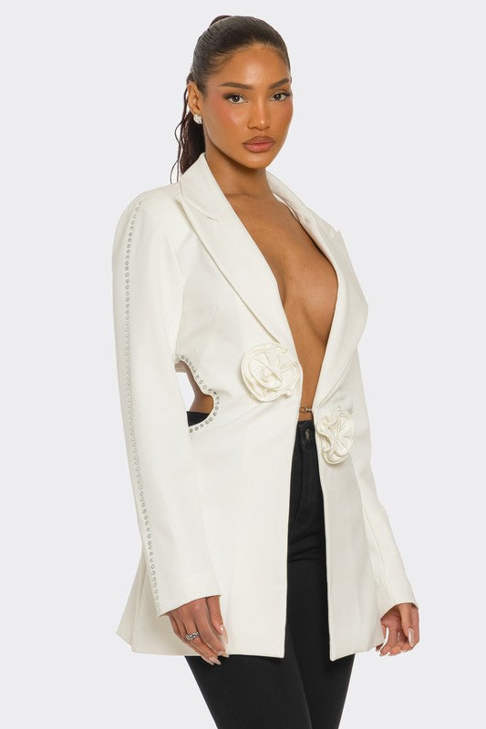 A lady posing in a sleek white blazer with floral details and a daring deep V-neckline, paired with black pants.