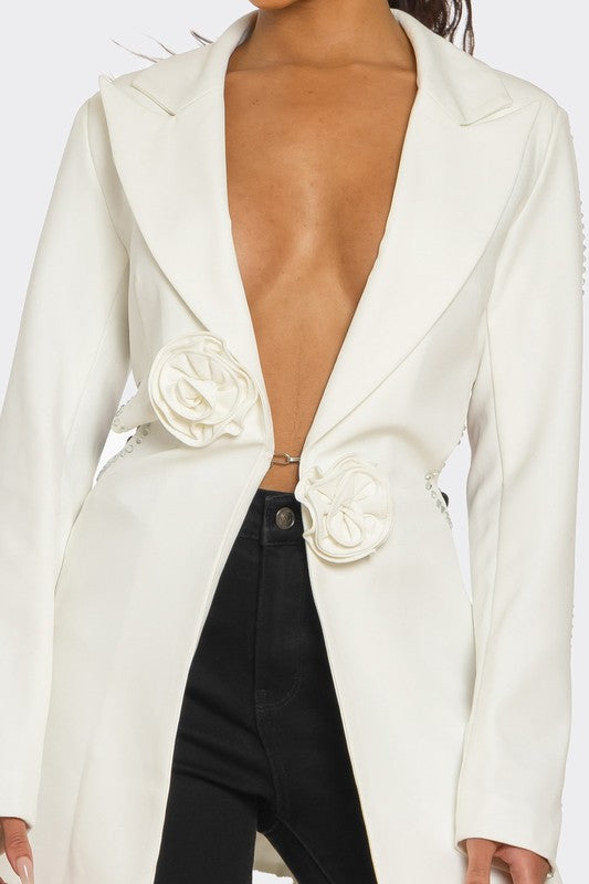 A lady posing in a sleek white blazer with floral details and a daring deep V-neckline, paired with black pants.