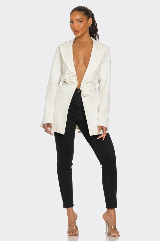 A lady posing in a sleek white blazer with floral details and a daring deep V-neckline, paired with black pants.