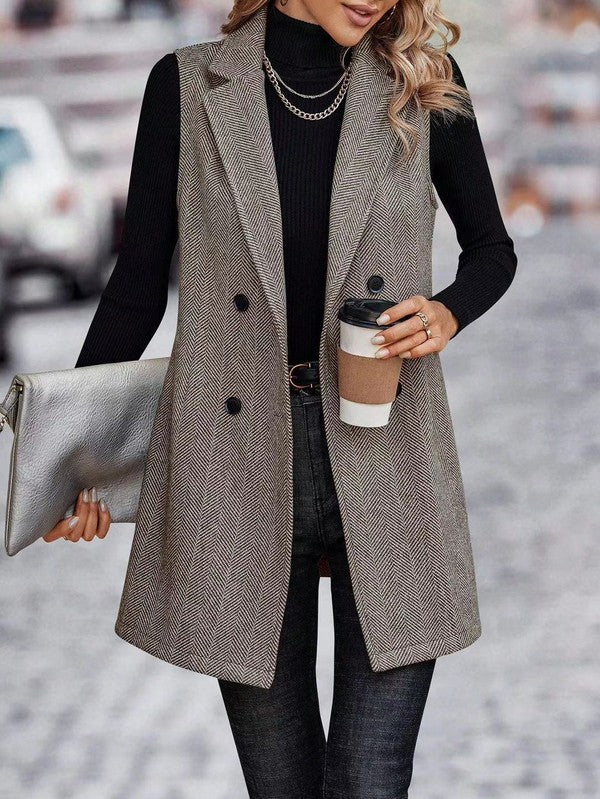A lady rocking a long gray vest over a black turtleneck and dark pants. She's holding a silver clutch in one hand and a coffee cup in the other.