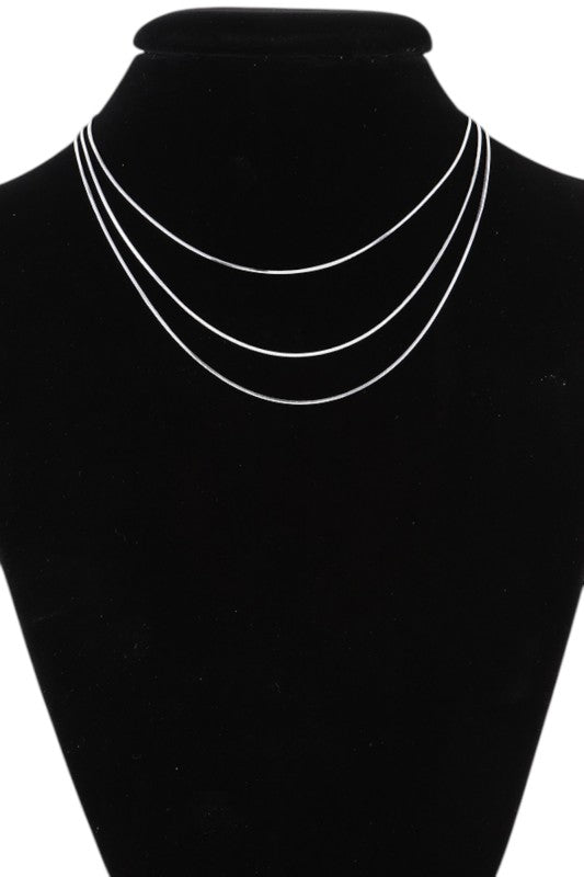 Layered gold necklace set displayed on black velvet, featuring three minimalist chains of varying lengths, perfect for a sleek, modern look.