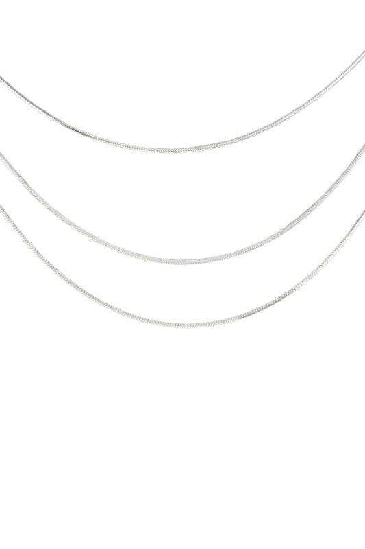 Layered gold necklace set displayed on black velvet, featuring three minimalist chains of varying lengths, perfect for a sleek, modern look.