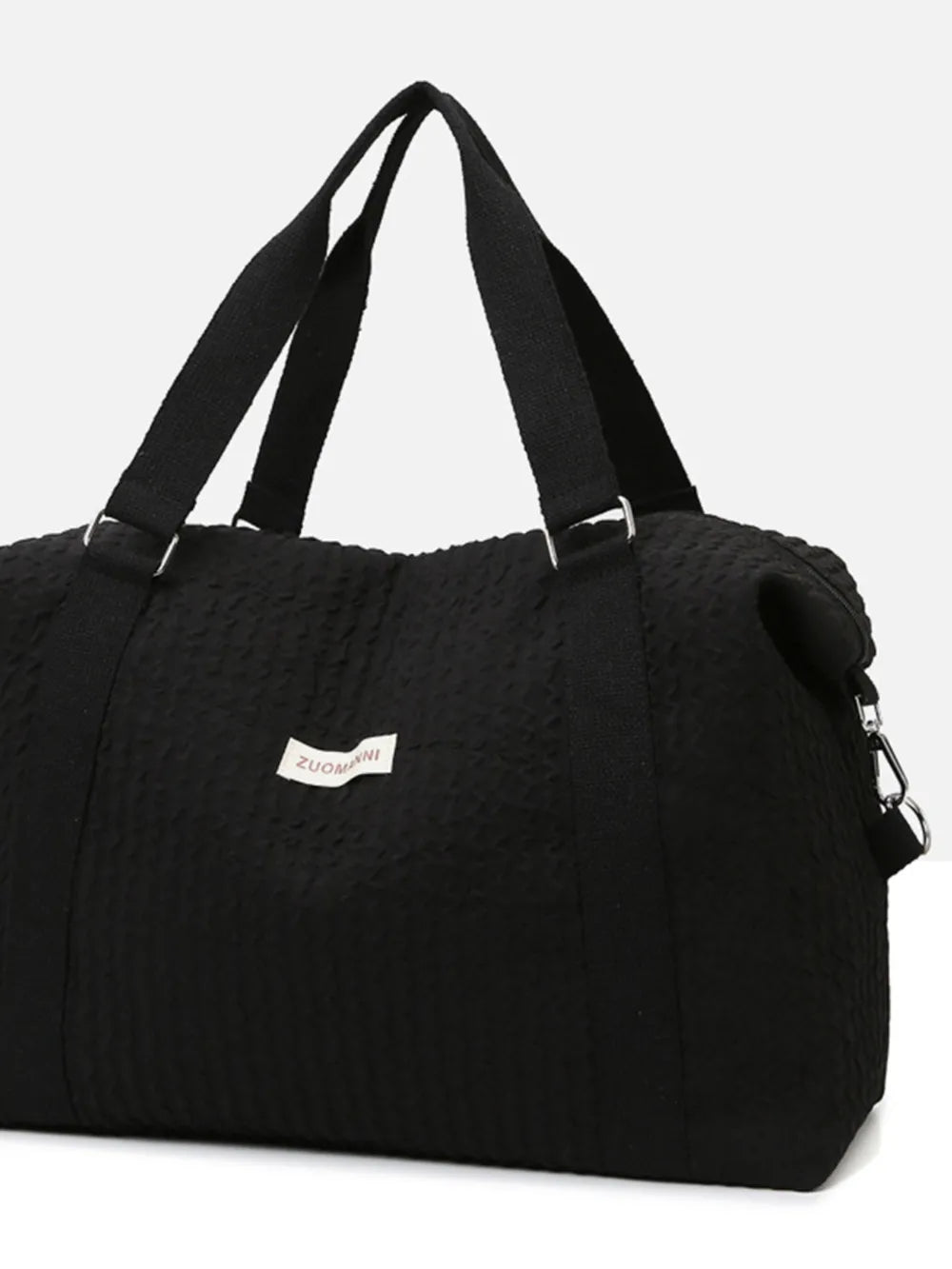 Black textured duffel bag with top handles and a detachable shoulder strap, featuring a small white label.  Set against a plain white background—sleek and minimal design.