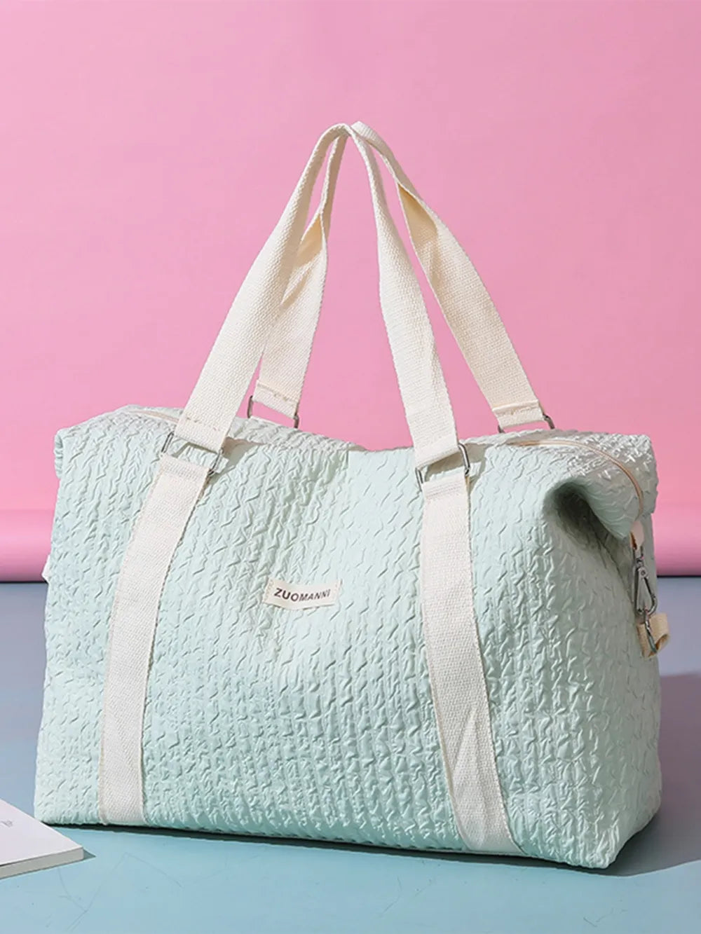 Light  mint green duffel bag with cream-colored handles and shoulder straps, featuring a crinkled texture and a front label. Soft, functional design—ideal for travel, gym, or everyday use.