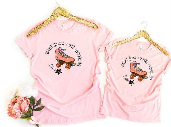 Two pink t-shirts with a roller skate graphic and text on hangers with gold trim.