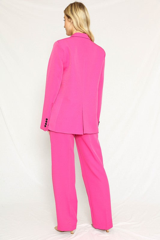 A woman rocking a hot pink suit with a blazer and matching pants. She's got long blonde hair and the suit has black buttons.