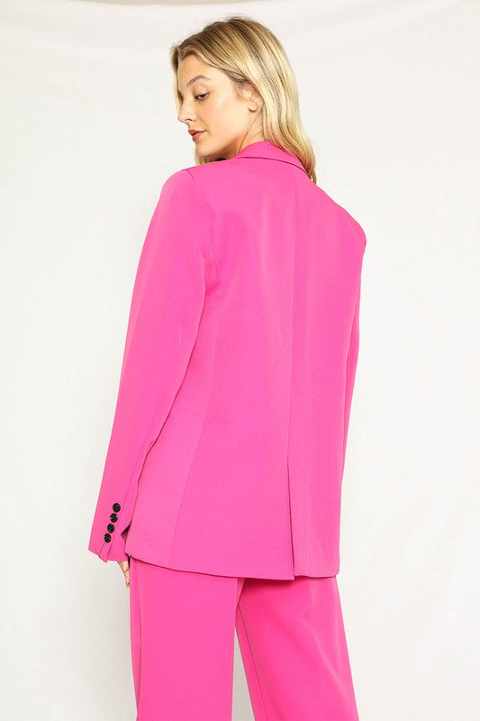 A woman rocking a hot pink suit with a blazer and matching pants. She's got long blonde hair and the suit has black buttons.