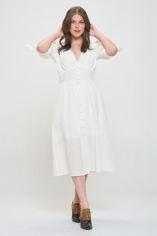 Woman wearing a white textured button-down midi dress with ¾ puff sleeves and tie detail.