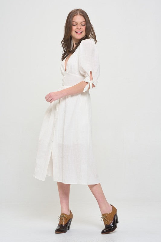 Woman wearing a white textured button-down midi dress with ¾ puff sleeves and tie detail.