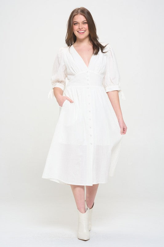 Woman wearing a white textured button-down midi dress with ¾ puff sleeves and tie detail.