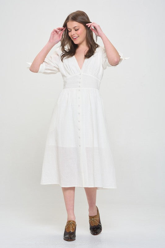 Woman wearing a white textured button-down midi dress with ¾ puff sleeves and tie detail.