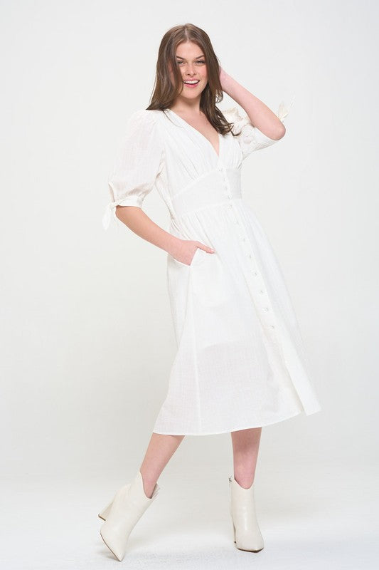 Woman wearing a white textured button-down midi dress with ¾ puff sleeves and tie detail.