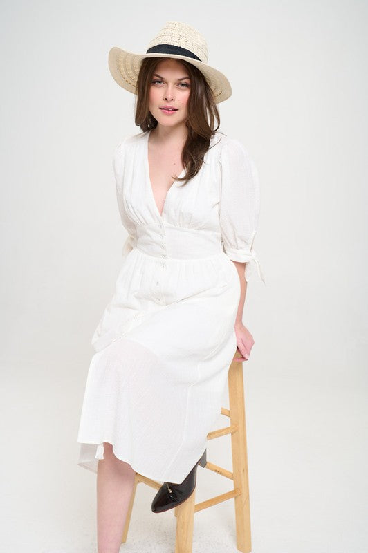 Woman wearing a white textured button-down midi dress with ¾ puff sleeves and tie detail.