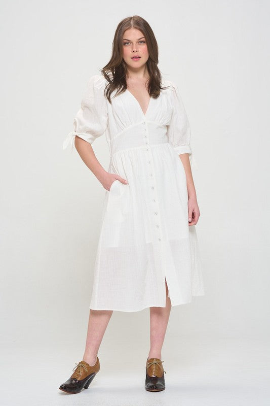 Woman wearing a white textured button-down midi dress with ¾ puff sleeves and tie detail.