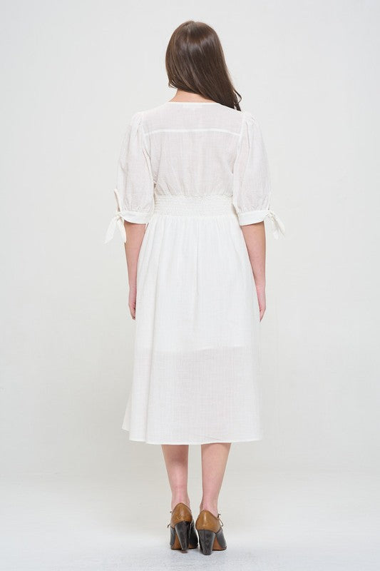 Woman wearing a white textured button-down midi dress with ¾ puff sleeves and tie detail.