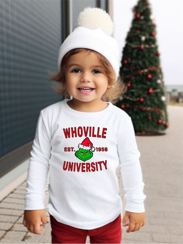 Child wearing a white sweatshirt with 'WHOVILLE UNIVERSITY' text, standing in front of a Christmas tree.