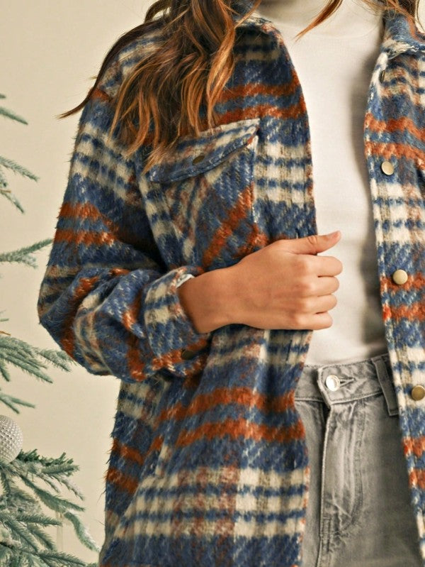 Person wearing a plaid coat with blue, orange, and beige colors, standing next to a Christmas tree wearing grey jeans