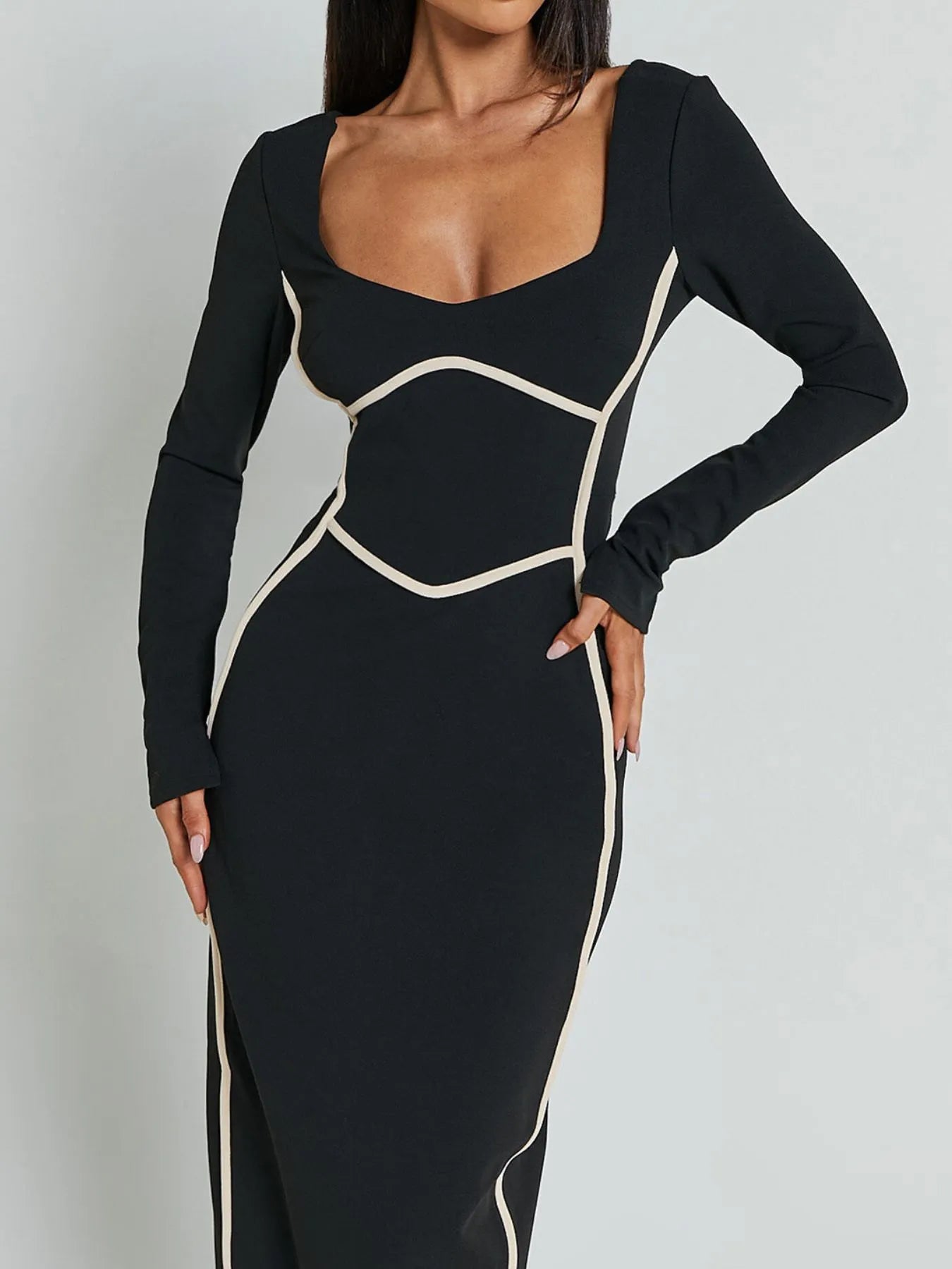 A full length form black dress with long sleeves and white trim details and has a geometric white pattern around the waist and shoulders