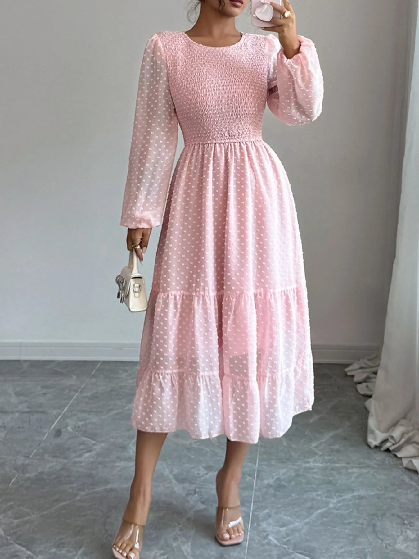 A pink dress features a fitted bodice with long sheer sleeves and a tiered flowing skirt that falls tomid-calf.
