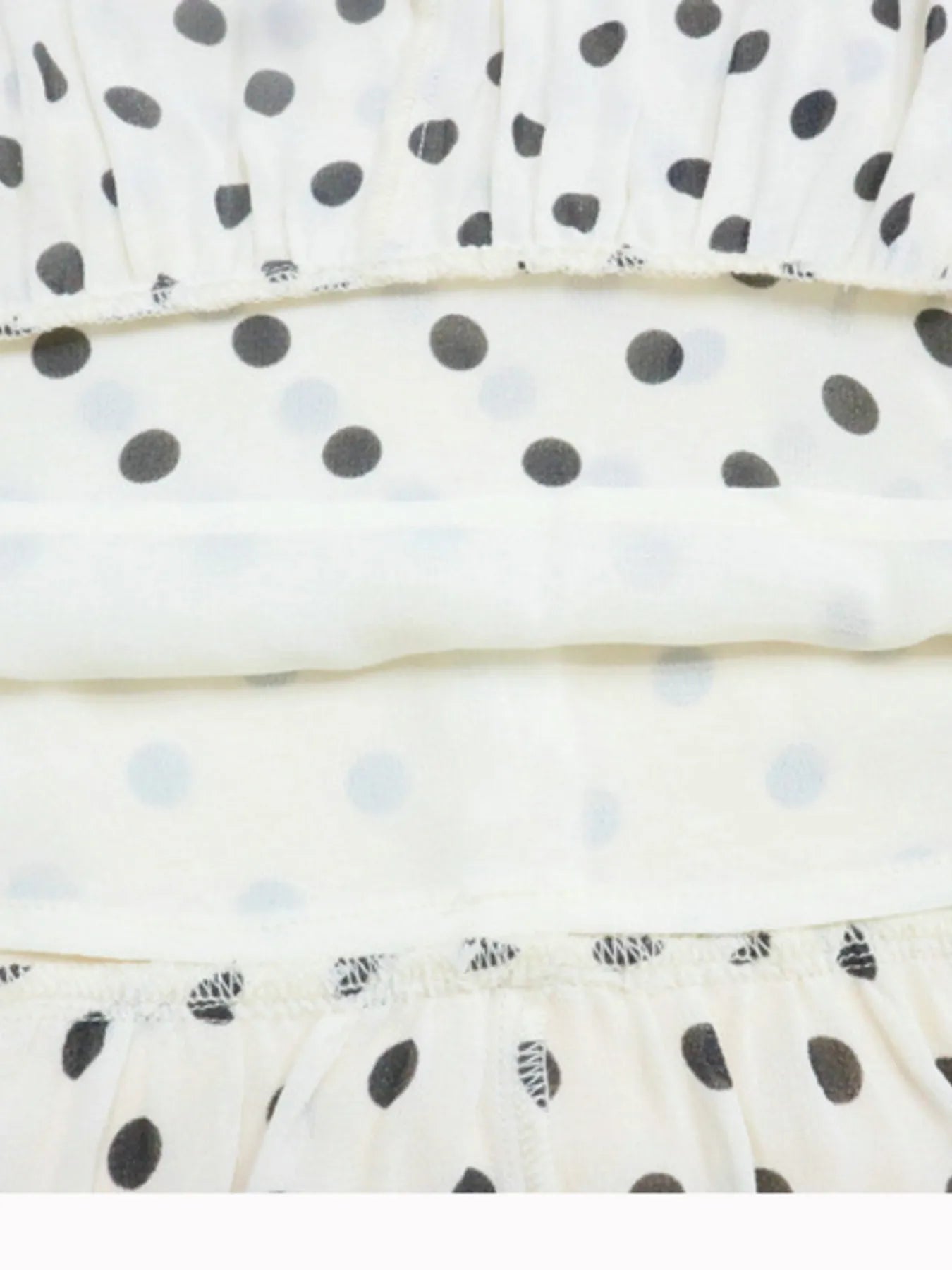 A white, polka-dotted, sleeveless maxi with a fitted bodice and a flared, ruffled hem that reaches the ankles