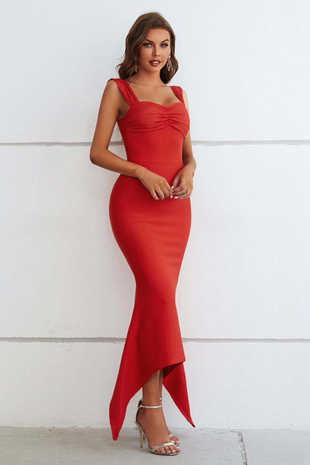A form-fitting, sleeveless red dress with a sweetheart neckline that hugs the figure and falls to a subtle, asymmetric hemline, creating an elegant and sexy silhouette.