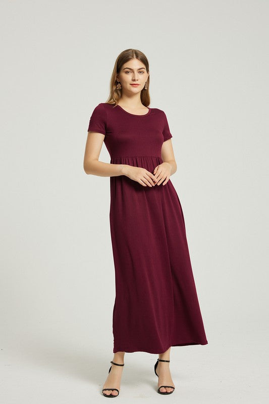 A woman in a maroon dress sits on a wooden chair with a black backrest, posing against a plain background.