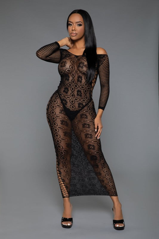 The dress is a form-fitting, full-length black lace bodysuit with long sleeves and a sheer, intricate pattern that reveals the silhouette underneath, paired with open-toe heels for a sultry, elegant look.