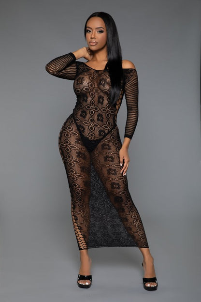 The dress is a form-fitting, full-length black lace bodysuit with long sleeves and a sheer, intricate pattern that reveals the silhouette underneath, paired with open-toe heels for a sultry, elegant look.