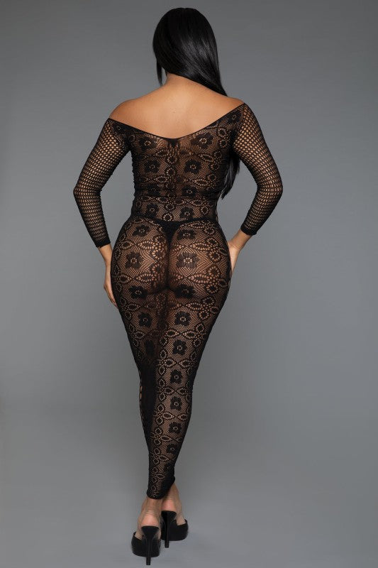 The dress is a form-fitting, full-length black lace bodysuit with long sleeves and a sheer, intricate pattern that reveals the silhouette underneath, paired with open-toe heels for a sultry, elegant look
