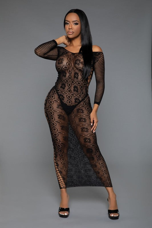 The dress is a form-fitting, full-length black lace bodysuit with long sleeves and a sheer, intricate pattern that reveals the silhouette underneath, paired with open-toe heels for a sultry, elegant look.