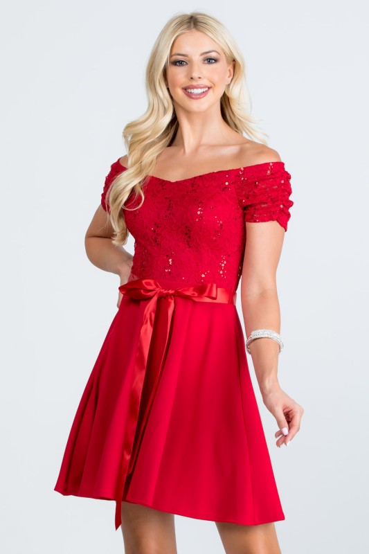 The dress is a knee-length, red frock with a fitted, off-the-shoulder bodice adorned with delicate lace or textured fabric and a full, flowing skirt tied at the waist with a matching sash.
