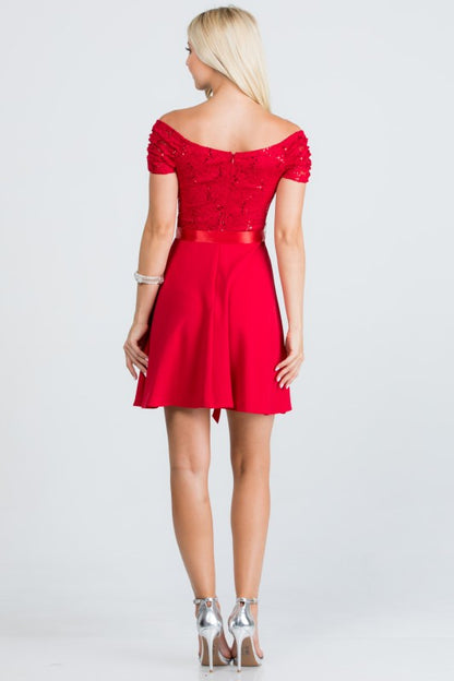 The dress is a knee-length, red frock with a fitted, off-the-shoulder bodice adorned with delicate lace or textured fabric and a full, flowing skirt tied at the waist with a matching sash.
