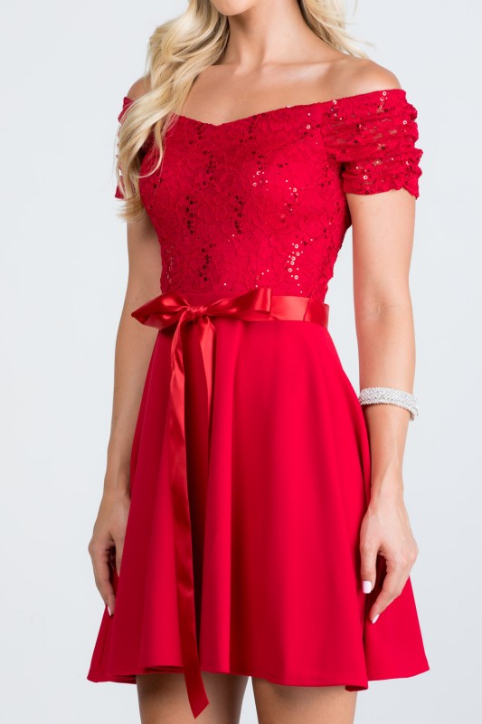 The dress is a knee-length, red frock with a fitted, off-the-shoulder bodice adorned with delicate lace or textured fabric and a full, flowing skirt tied at the waist with a matching sash.