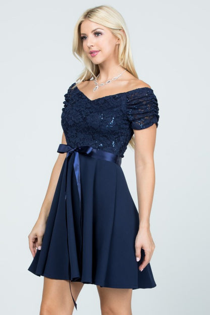 The dress is a navy blue, off-the-shoulder fit-and-flare style with a lace bodice and a satin ribbon belt at the waist.