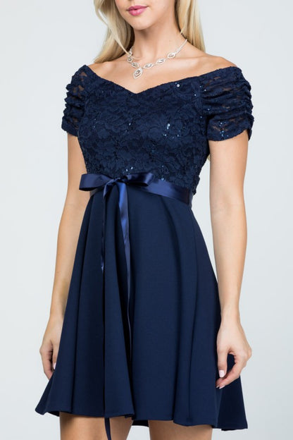 The dress is a navy blue, off-the-shoulder fit-and-flare style with a lace bodice and a satin ribbon belt at the waist.