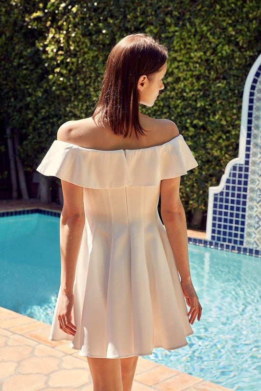 The dress is a short, off-the-shoulder white frock with a dramatic ruffled neckline and a flared, A-line skirt.