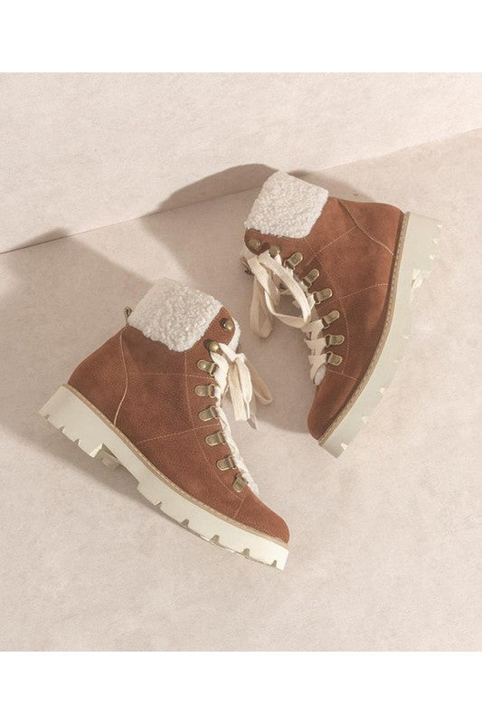 Brown suede hiking boots with white sherpa lining, lace-up front, gold eyelets, and chunky white lug sole.