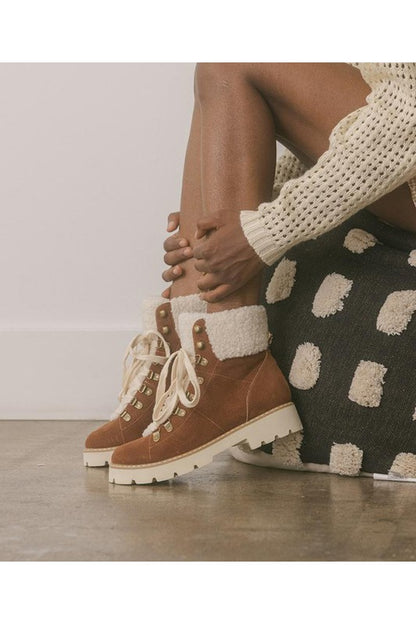 Brown suede hiking boots with white sherpa lining, lace-up front, gold eyelets, and chunky white lug sole.