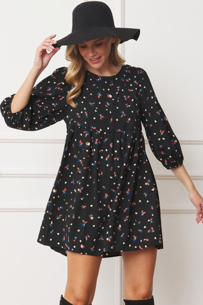 The dress is a short, loose-fitting black shift adorned with a delicate, colorful floral print and three-quarter sleeves