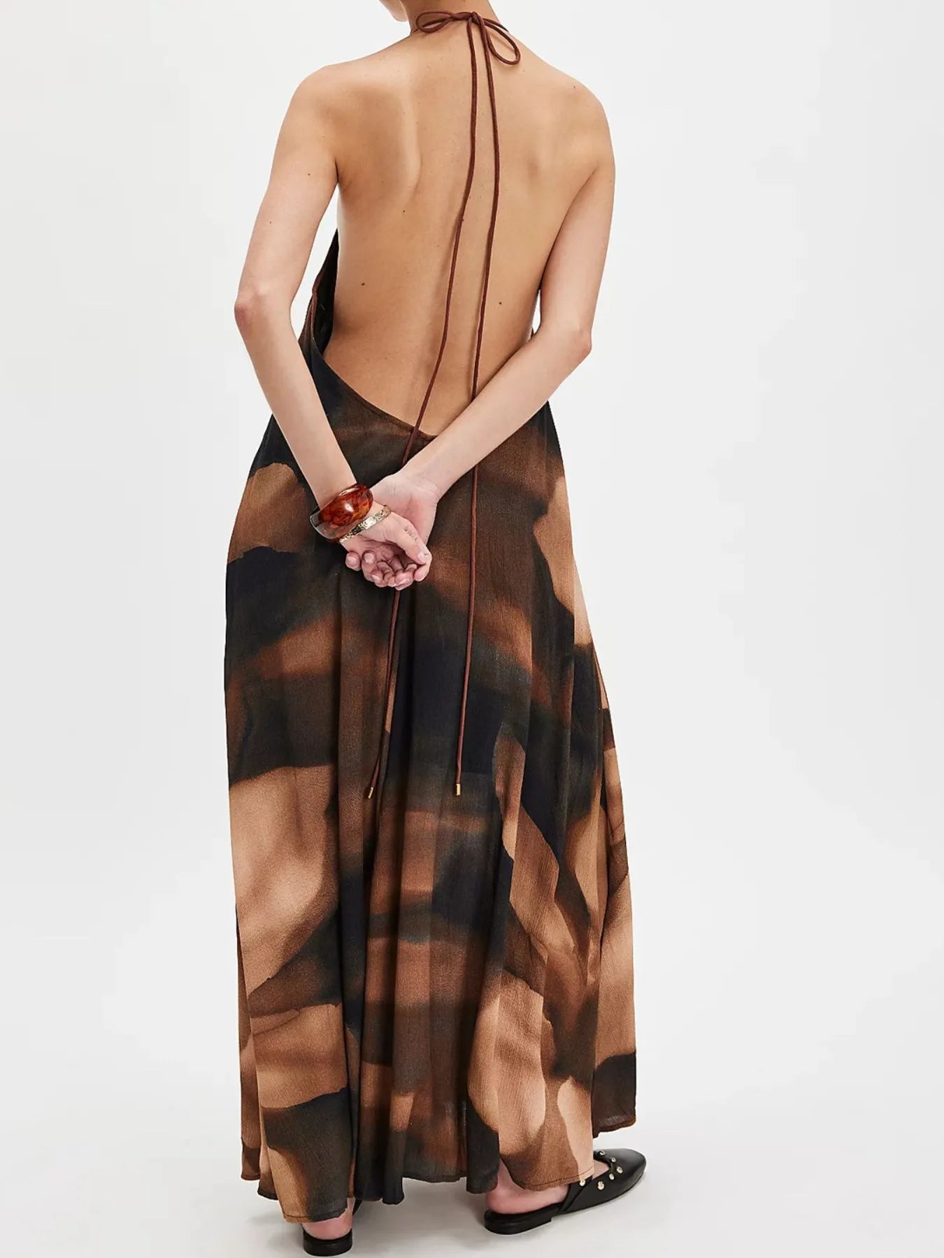 Woman wearing a flowing abstract print halter-neck maxi cami dress with deep neckline.