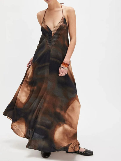 Woman wearing a flowing abstract print halter-neck maxi cami dress with deep neckline.