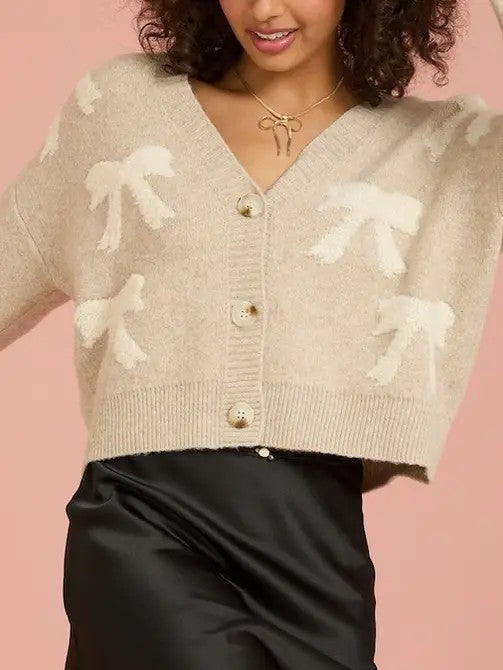 Person wearing a beige cardigan with white floral patterns on a pink background