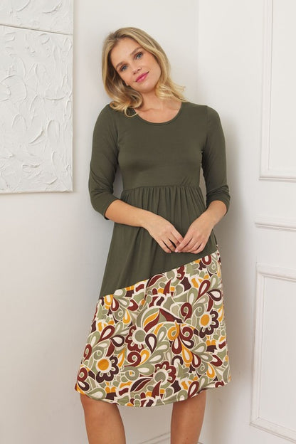 Woman wearing an olive green midi dress with a colorful, abstract floral or paisley pattern on the bottom half