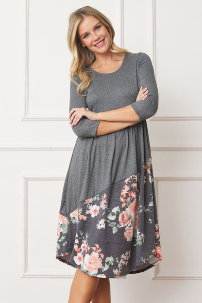 Woman wearing a gray midi dress with a floral pattern on the bottom half, with arms crossed.