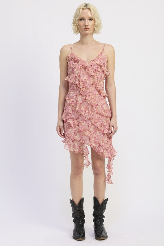 The dress is a pink, asymmetrical, ruffled mini dress with delicate spaghetti straps, featuring a loose, draped silhouette and a slightly sheer, layered texture that gives it a playful, feminine look.