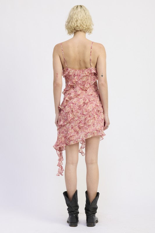 The dress is a pink, asymmetrical, ruffled mini dress with delicate spaghetti straps, featuring a loose, draped silhouette and a slightly sheer, layered texture that gives it a playful, feminine look.