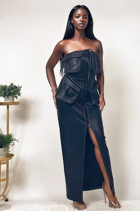 The dress is a sleek, off-shoulder, dark navy gown with a structured bodice, a dramatic draped overlay, and a high slit that reveals one leg.