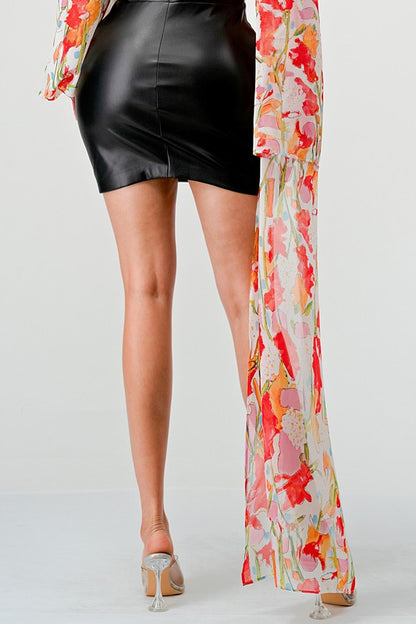 a woman in a black leather mini skirt and a floral print off-the-shoulder top with dramatic sleeves.